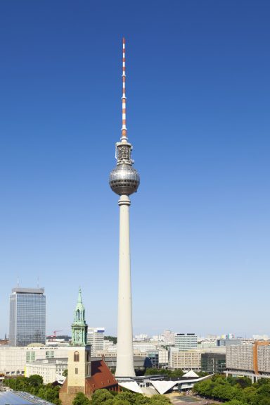Fernsehturm Berlin vor klarem Himmel, mit modernen Gebäuden im Hintergrund.