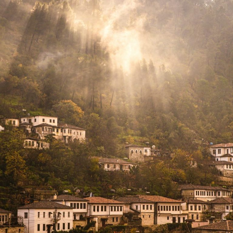 Bergdorf mit traditionellen Häusern, umgeben von nebligen Bergen und Sonnenstrahlen.