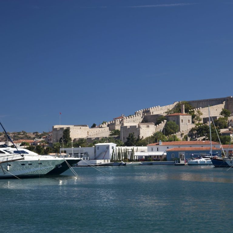 Hafen mit Yachten und Festung im Hintergrund, bei klarem blauen Himmel.