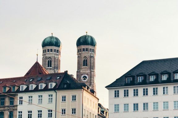 Zwei Türme mit grünen Kuppeln, flankiert von historischen Gebäuden in einer Stadt.
