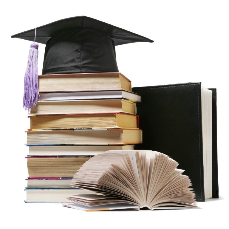 Hochschulabschlussmütze auf einem Stapel Bücher mit einem offenen Buch davor.