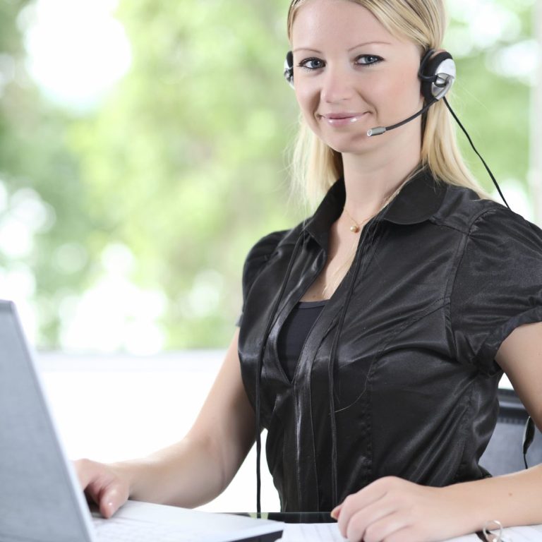 Frau mit Headset vor einem Laptop, lächelt freundlich.