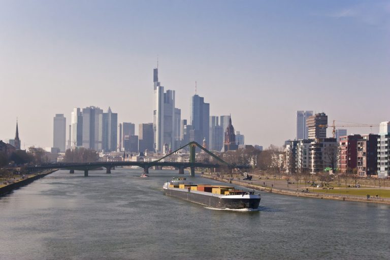 Blick auf den Fluss mit einem Schiff und der Skyline von Frankfurt im Hintergrund.