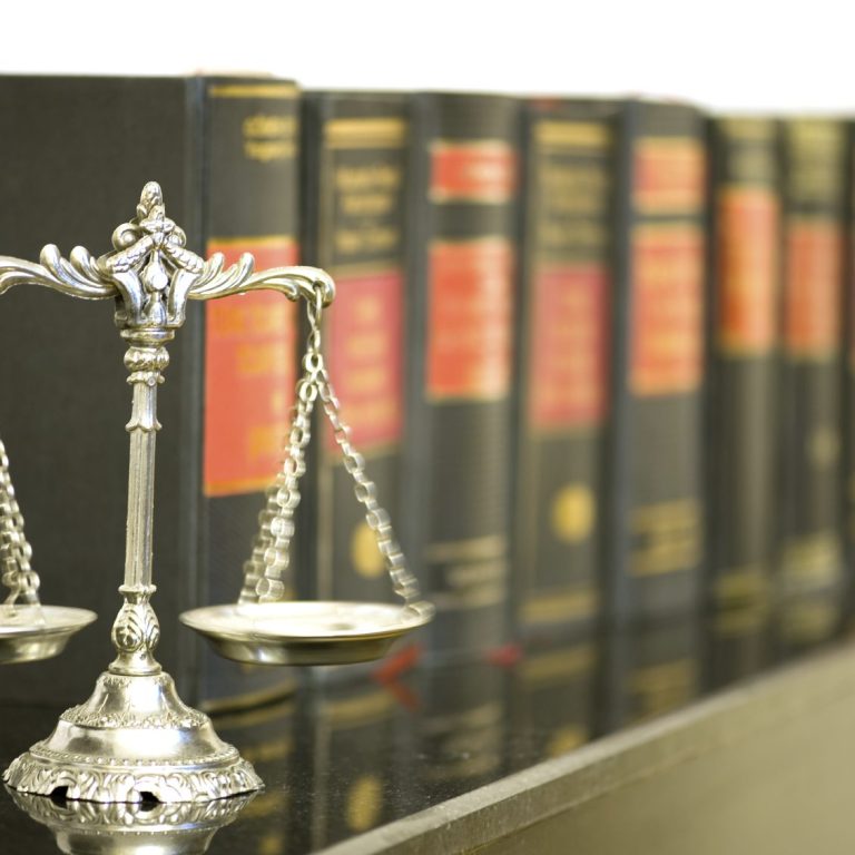 Silberne Waage vor Bücherregal mit juristischen Fachbüchern.