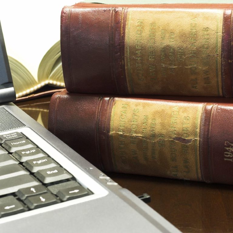 Laptop neben zwei alten, gebundenen Büchern auf einem Holztisch.
