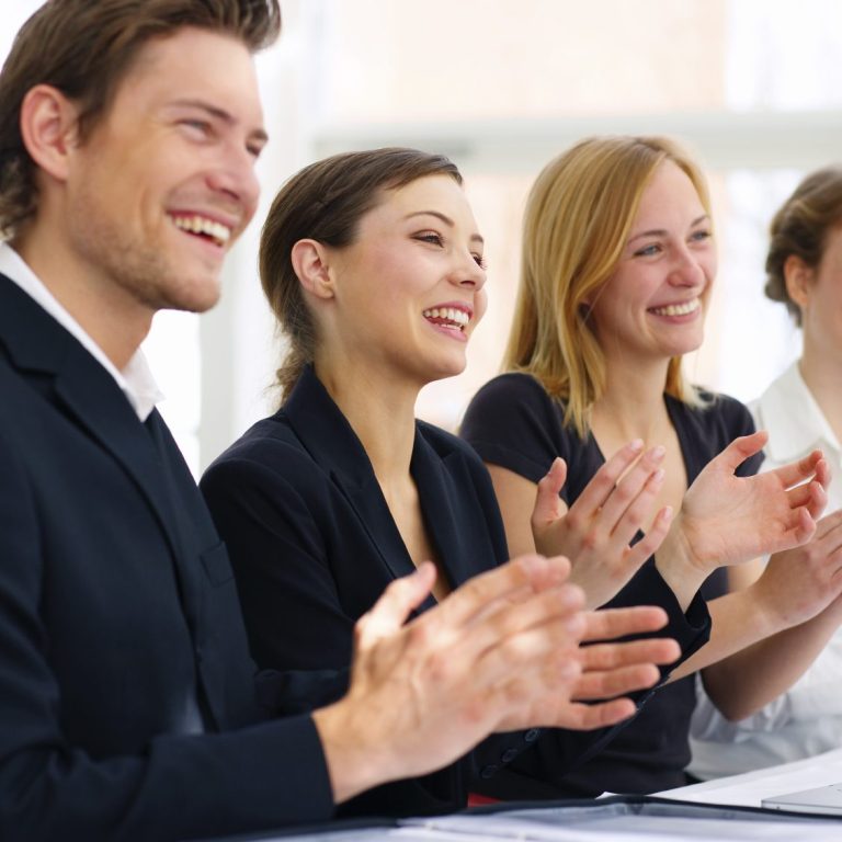 Vier Menschen applaudieren lächelnd während einer Präsentation oder Besprechung.