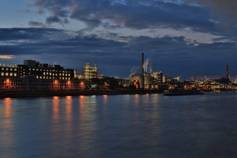 Städtische Skyline mit reflektierenden Lichtern am Wasser bei Dämmerung.