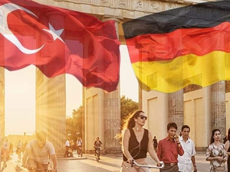 Frau mit Fahrrad vor dem Brandenburger Tor, umgeben von türkischer und deutscher Flagge.