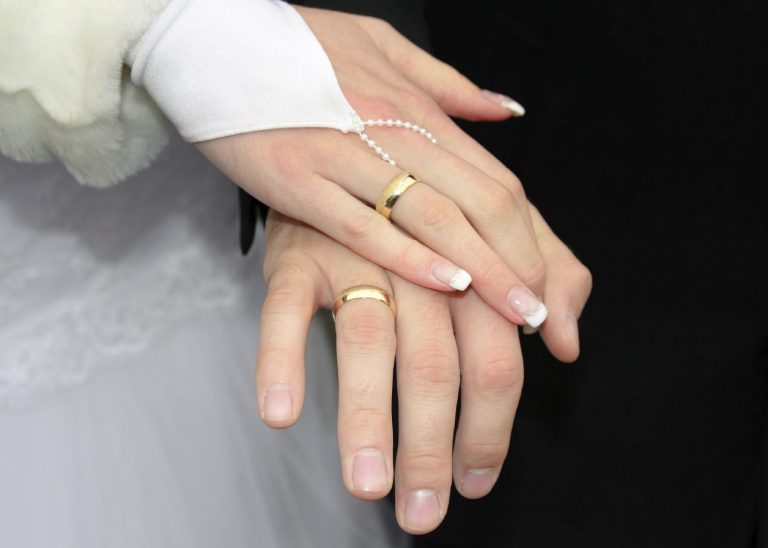 Hochzeitsringe an den Händen eines Paares, die sich liebevoll halten.