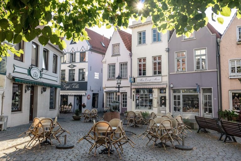 Gemütlicher Platz mit leeren Tischen und bunten Häusern in einer Stadt.
