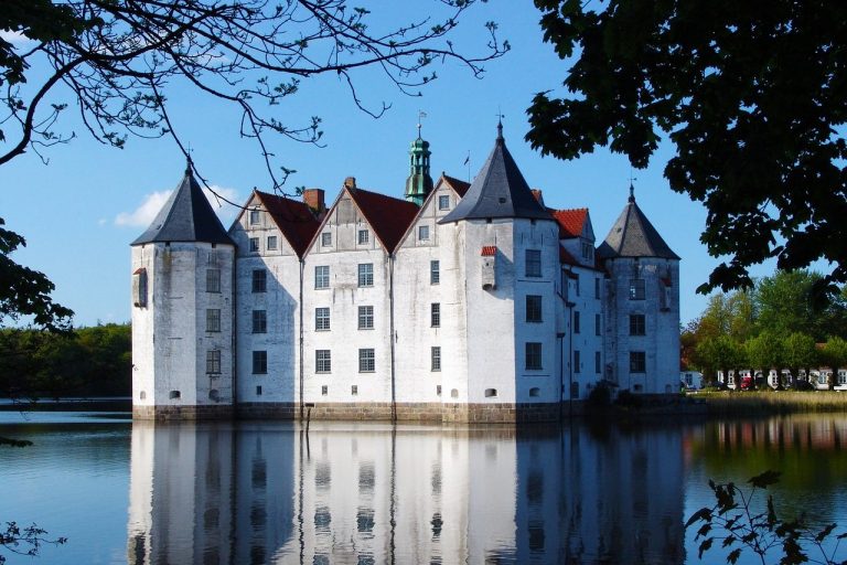 Schloss mit Türmen spiegelt sich im ruhigen Wasser eines Sees.
