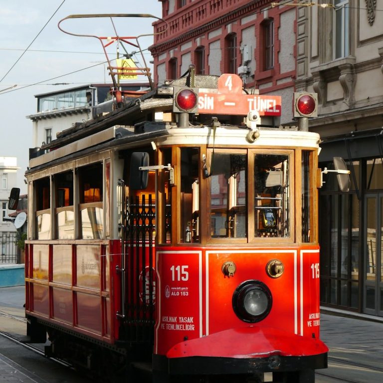 Rote Straßenbahn mit Holzkonstruktion auf einer urbanen Straße.