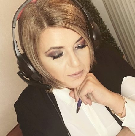 Frau mit Headset, nachdenklich, hält einen Stift und trägt ein elegantes Oberteil.