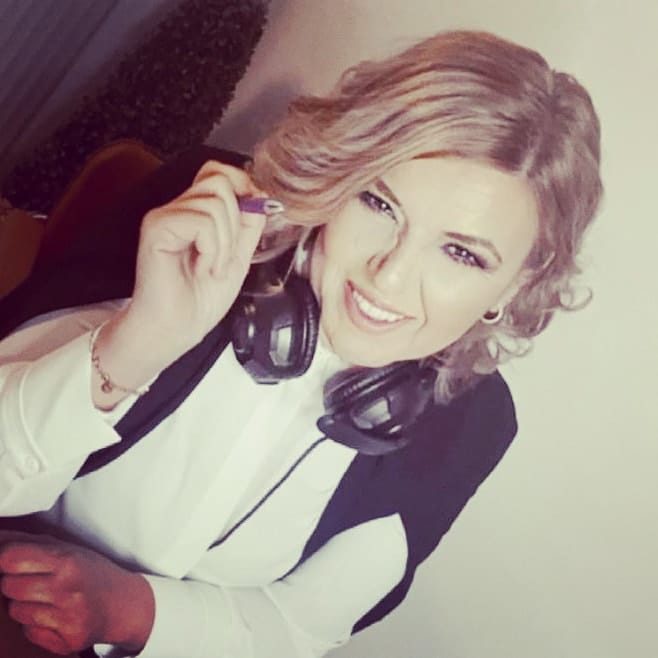 Frau mit lächelndem Gesicht, Kopfhörern um den Hals und blonden Locken.