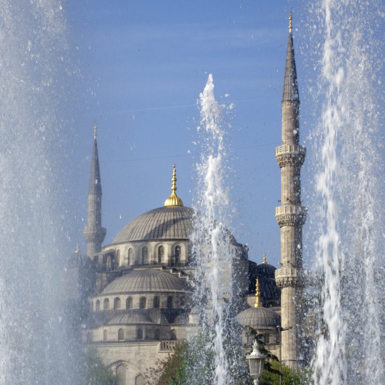 Blick auf die Sultan-Ahmed-Moschee hinter Wasserfontänen vor klarem Himmel.