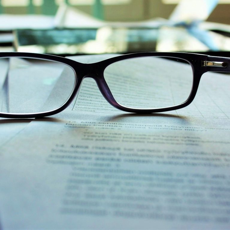 Schwarze Brille auf einem geöffneten Buch mit Text.
