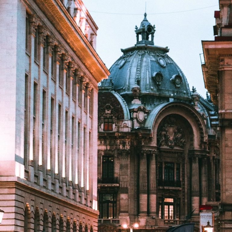 Historische Gebäude mit gewölbtem Dach und Säulen in einer urbanen Umgebung.