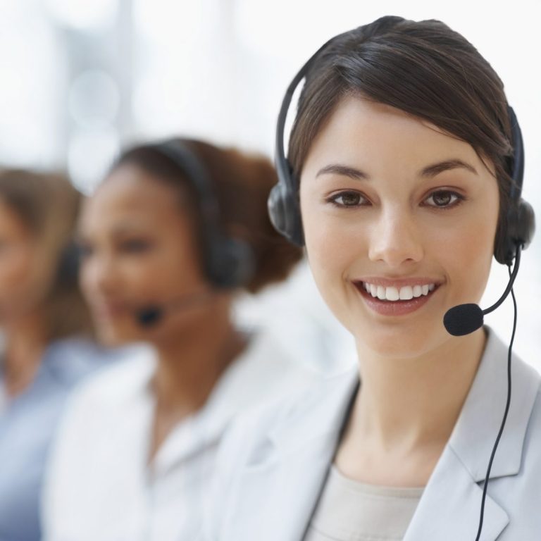 Lächelnde Frau mit Headset, im Hintergrund weitere Personen im Callcenter.