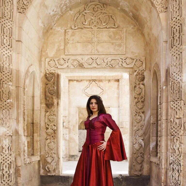 Frau in rotem Kleid steht in einem historischen, verzierten Bauwerk.