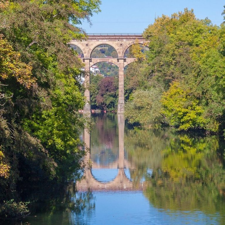 Bautzen-Aquädukt, umgeben von Bäumen, spiegelt sich im ruhigen Wasser.