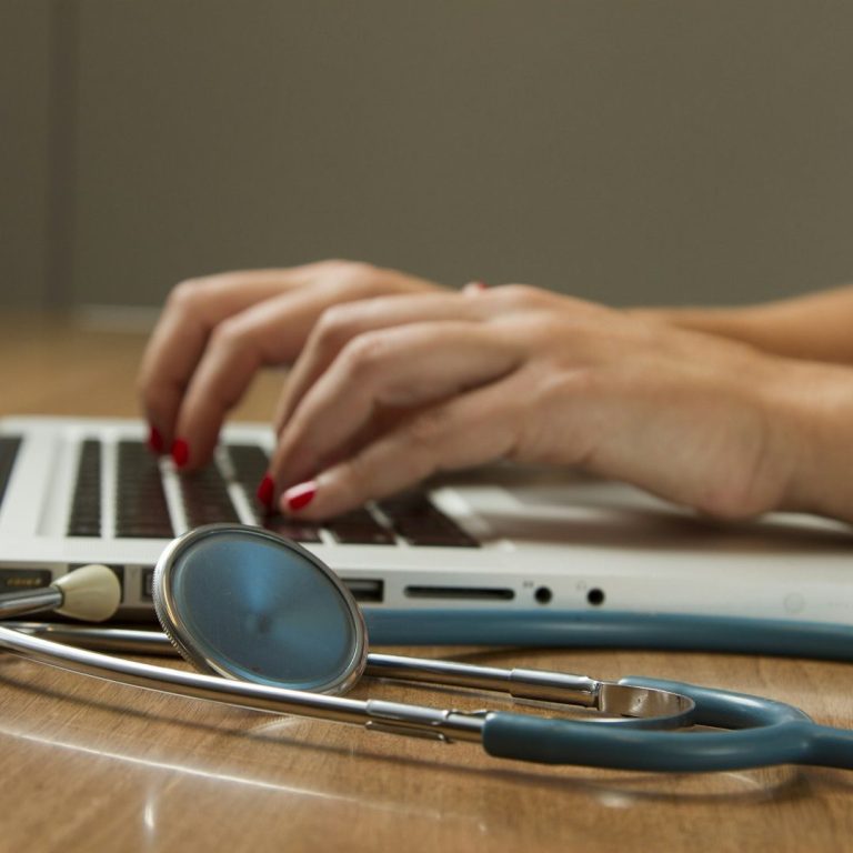 Hände tippen auf Laptop mit Stethoskop im Vordergrund – Symbolbild für Türkisch–Deutsch Übersetzungen medizinischer Unterlagen, Atteste 