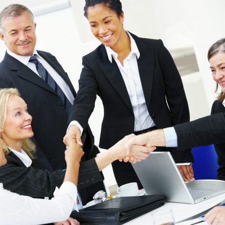 Fünf Personen in Businesskleidung schütteln sich die Hände bei einem Meeting.