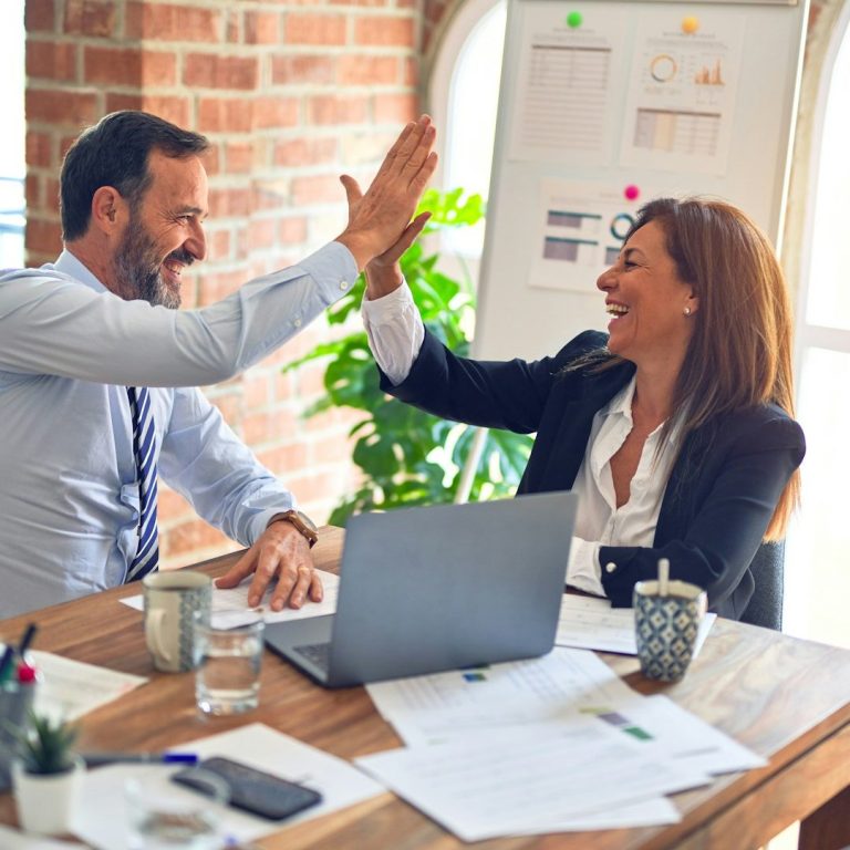 Geschäftsfrau und Geschäftsmann geben sich im Büro ein High-Five – erfolgreiche Zusammenarbeit dank professioneller Dolmetschdienste