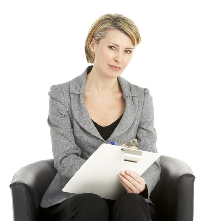 Frau in grauem Blazer sitzt auf einem Stuhl mit einem Notizblock.