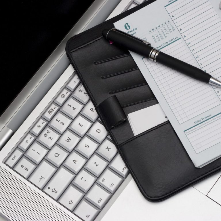 Schwarze Mappe mit Stift und Notizblock auf einer Laptop-Tastatur.