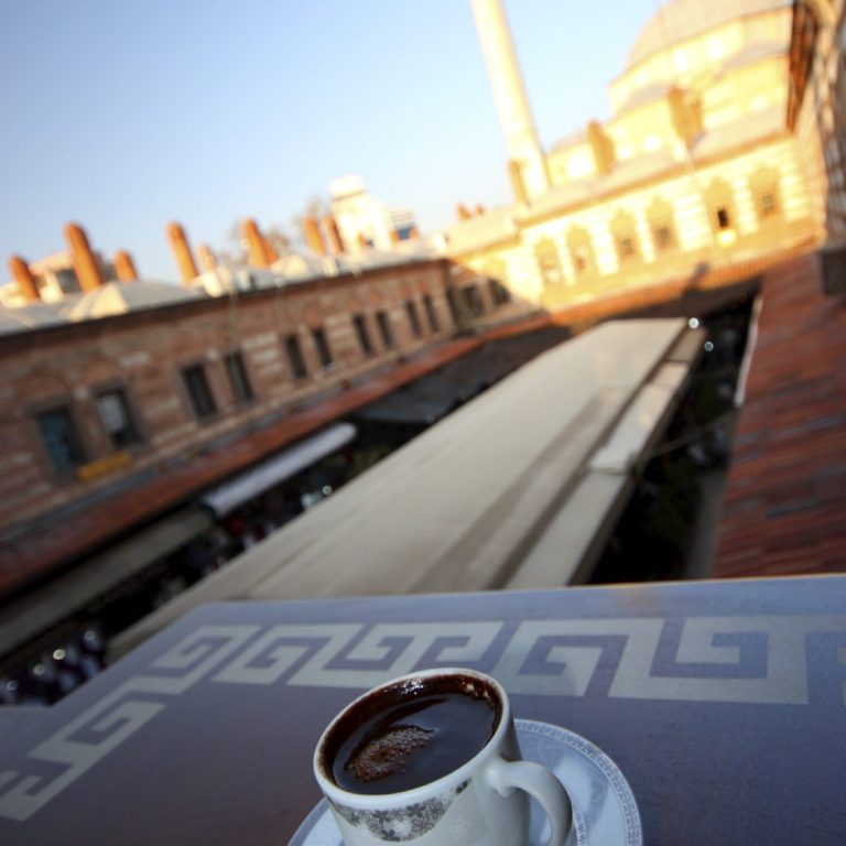 Tasse Kaffee auf einem Tisch, Blick auf historische Architektur und Menschenmenge.