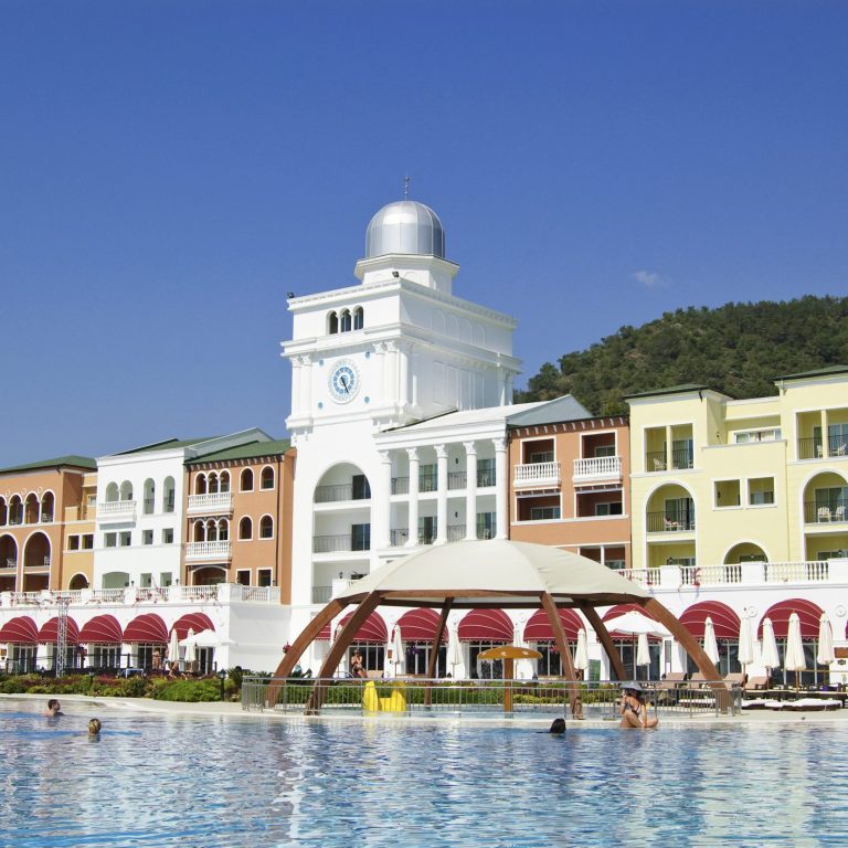 Blick auf ein farbenfrohes Hotel mit Pool und umliegenden Bergen.