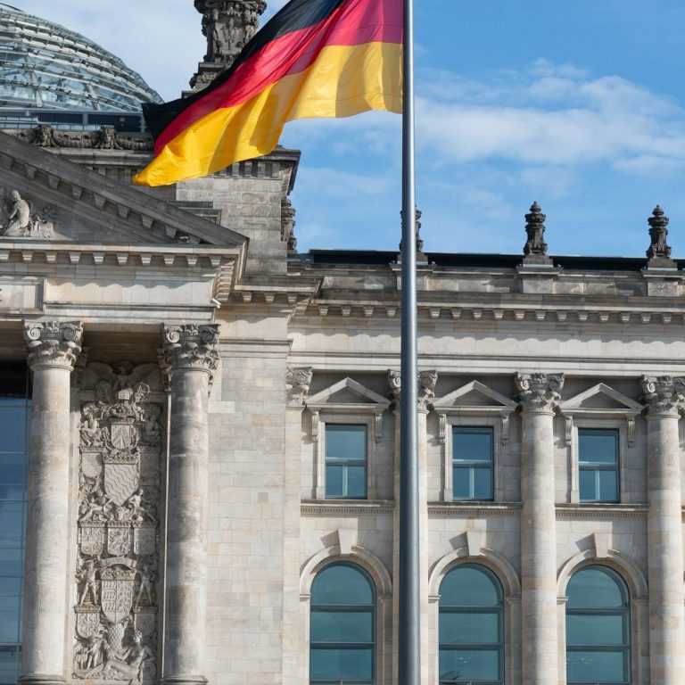 Deutsche Flagge vor dem Reichstagsgebäude in Berlin bei klarem Himmel.
