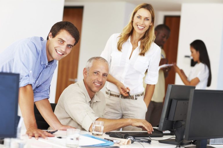 Gruppe von vier Personen in einem modernen Büro, die an Computern arbeiten und lächeln.
