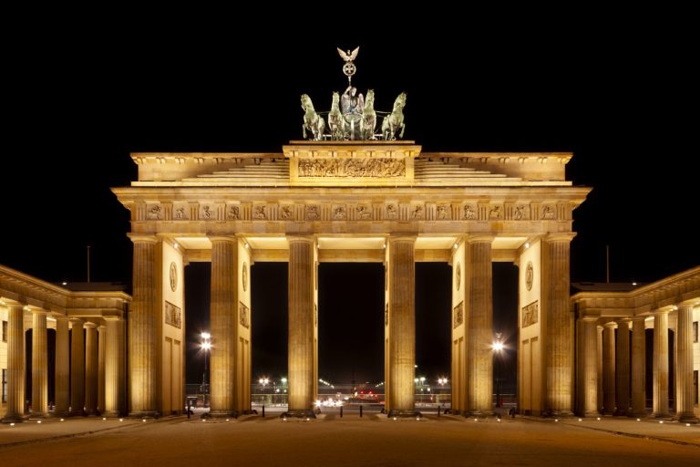 Das Brandenburger Tor beleuchtet bei Nacht, umgeben von Straßen und städtischer Beleuchtung.