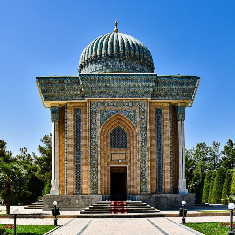 Historisches Mausoleum mit blauer Kuppel und farbenfrohen Fliesen, umgeben von Gärten.