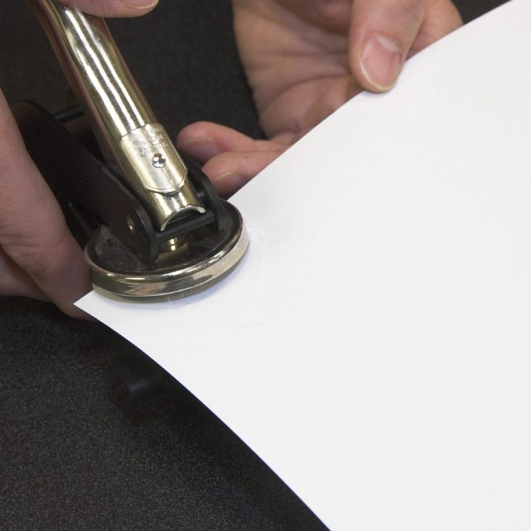 Eine Hand hebt einen Locher über ein Blatt Papier.