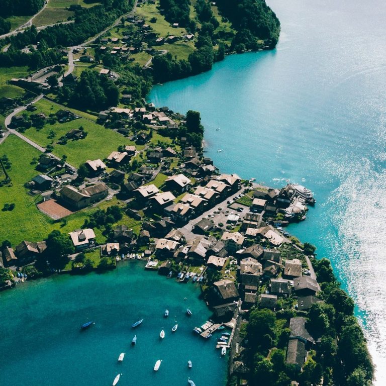 Landschaft mit einem idyllischen See, umgeben von grünen Hügeln und kleinen Dörfern.
