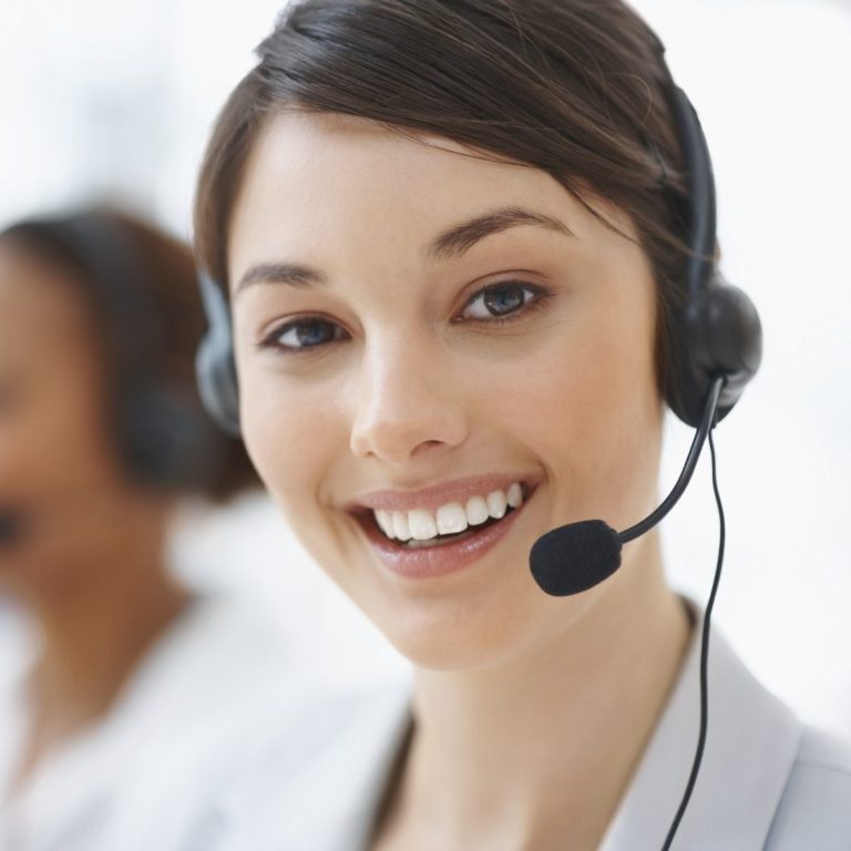 Lächelnde Frau mit Headset in einem Büro, Hintergrund unscharf.