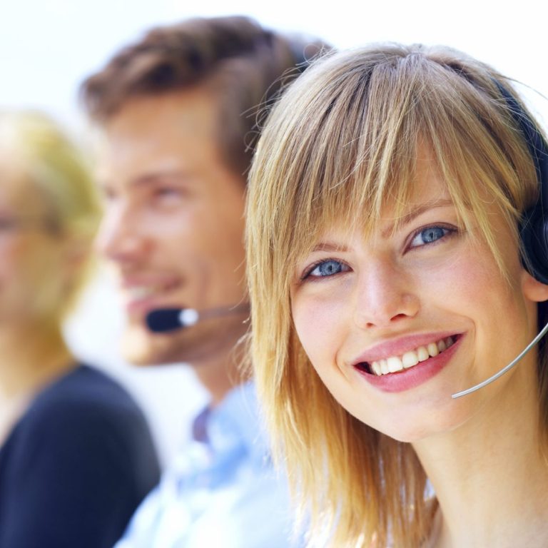 Lächelnde Frau mit Headset, begleitet von zwei Personen im Hintergrund.