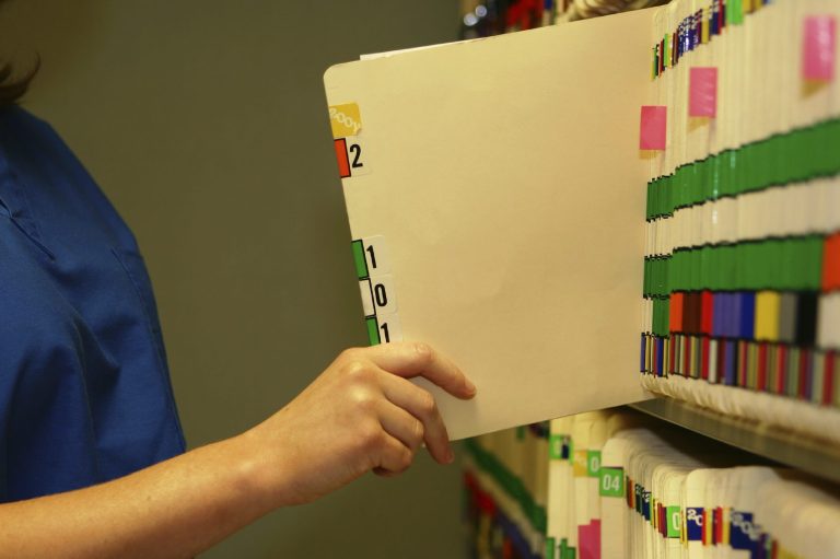 Eine Hand hält eine leere Registerkarte vor farblich gekennzeichneten Akten.